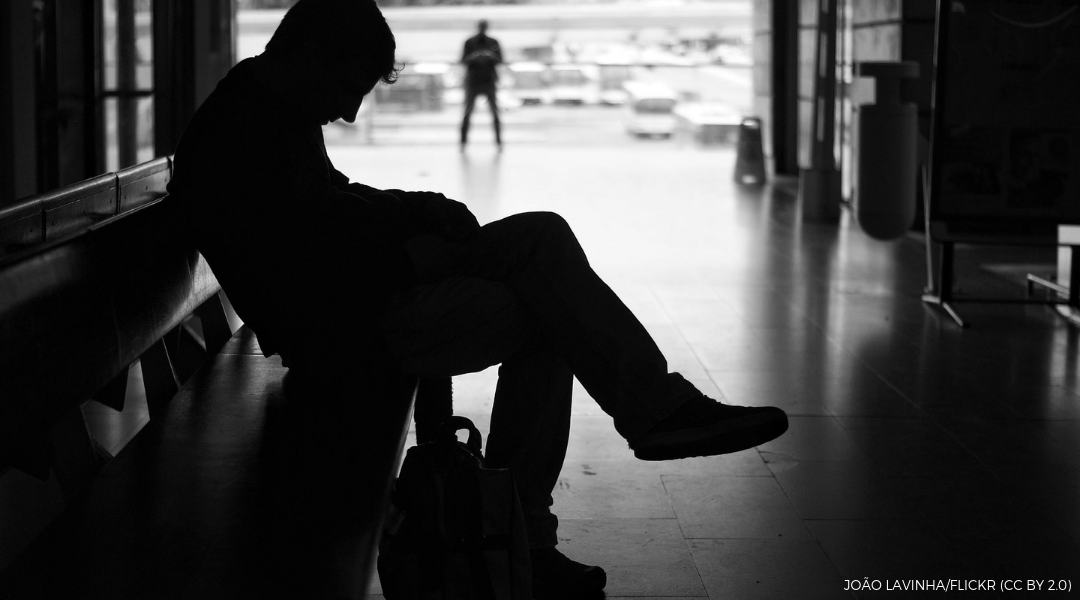 Homeless young male sitting on a bench with head down in a shadow silhouette