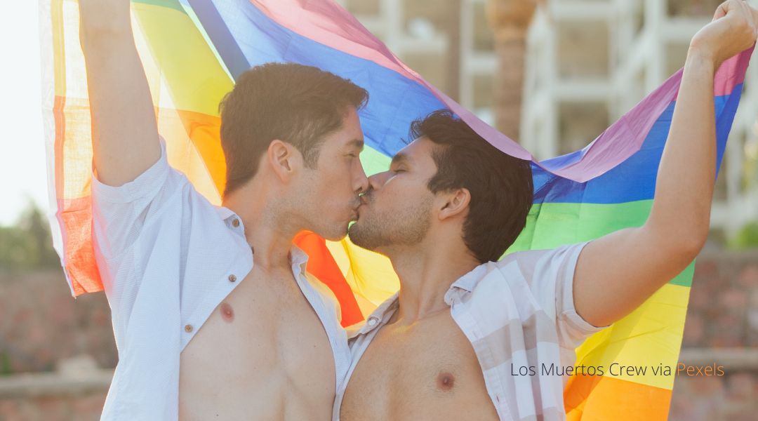 Two men kissing under a pride flag