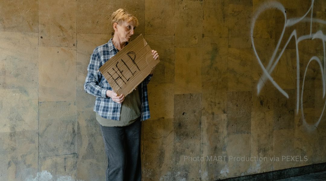 an unstably housed woman holding a sign reading HELP